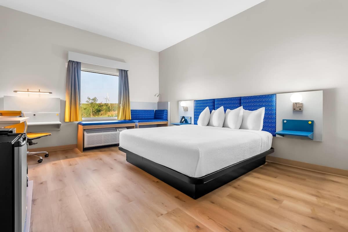 Quarto de hotel moderno com uma cama grande, uma escrivaninha e vista para o exterior.