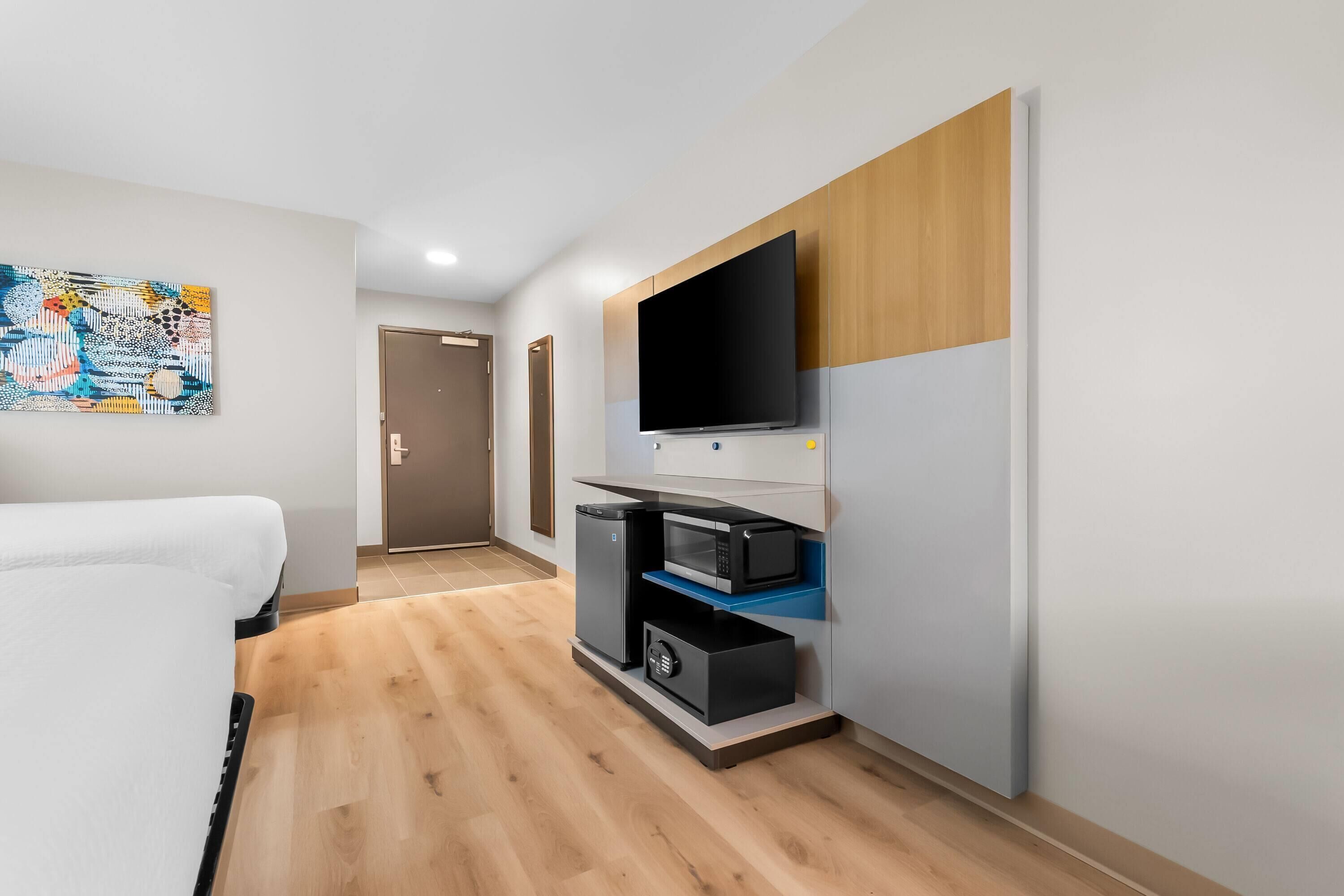 A hotel room with a bed, a TV mounted on a wall, a microwave, and a small refrigerator.