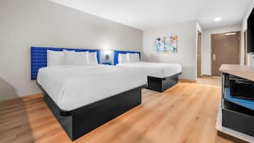 A modern hotel room with a large bed, a desk, and a small kitchenette.