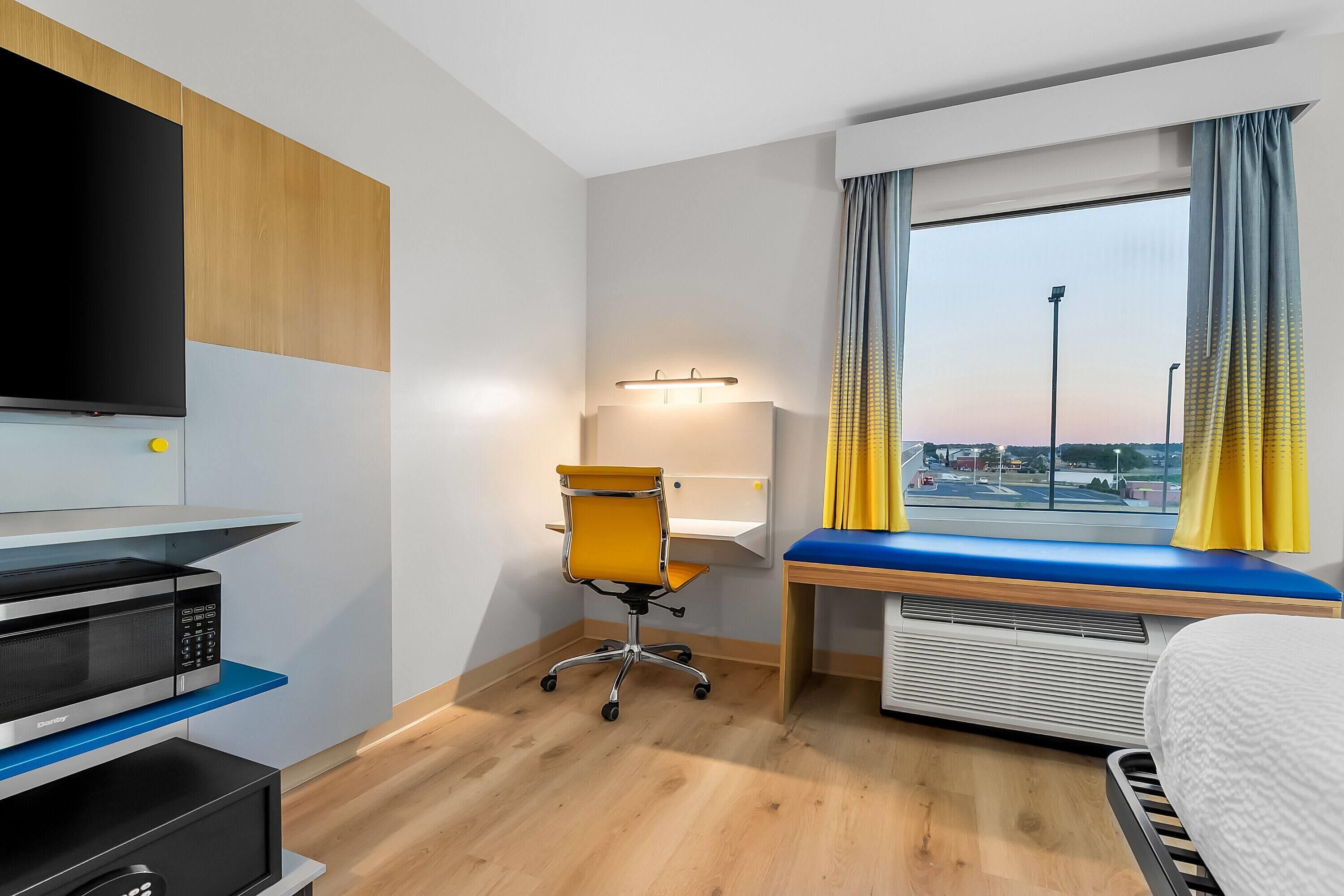 Ein Hotelzimmer mit einem Bett, einem Schreibtisch mit blauer Auflage, einem Sessel, einem Flachbildfernseher, einer Mikrowelle und einem Heizgerät.