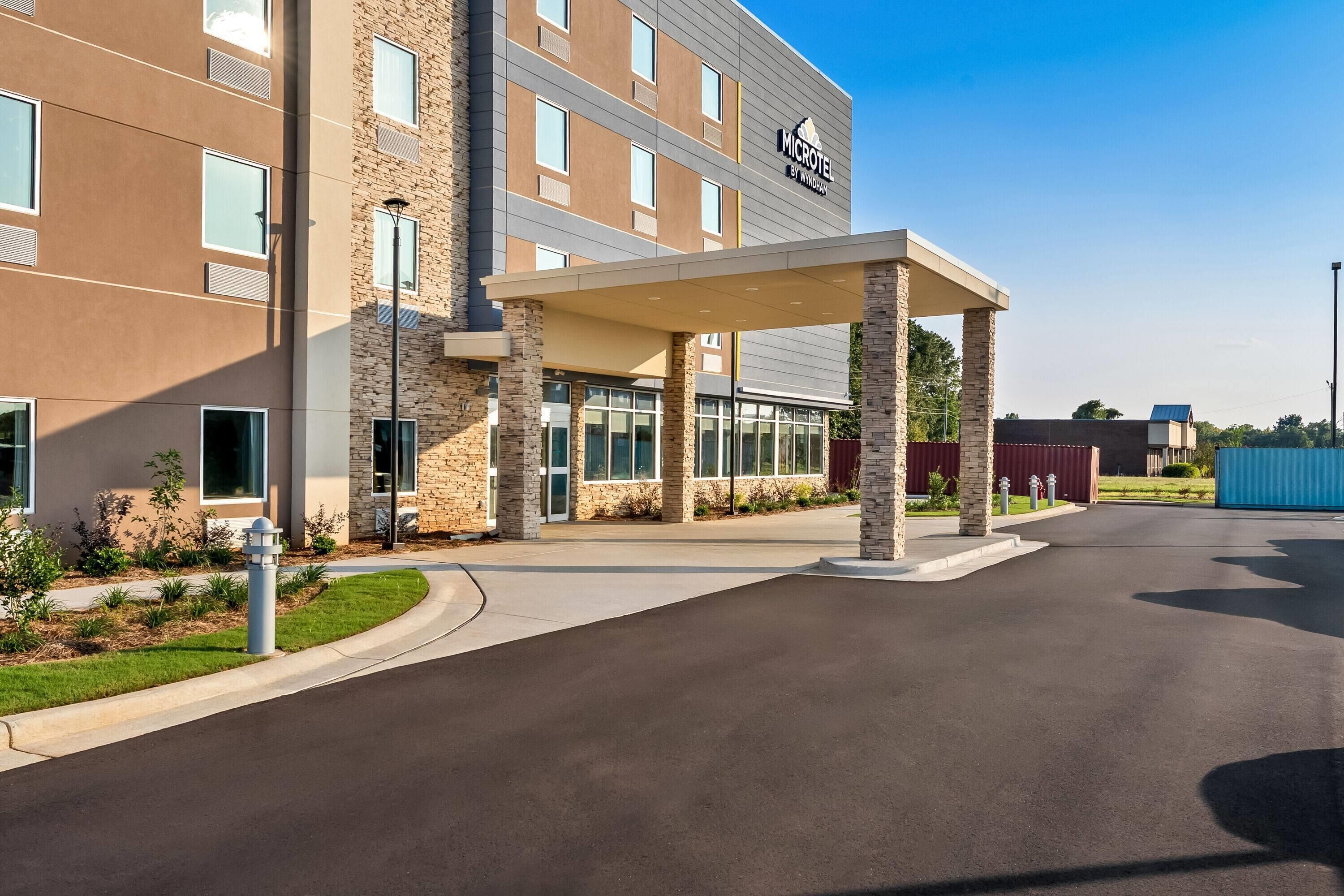 A modern hotel entrance with a covered walkway, stone facade, and a clear sky.