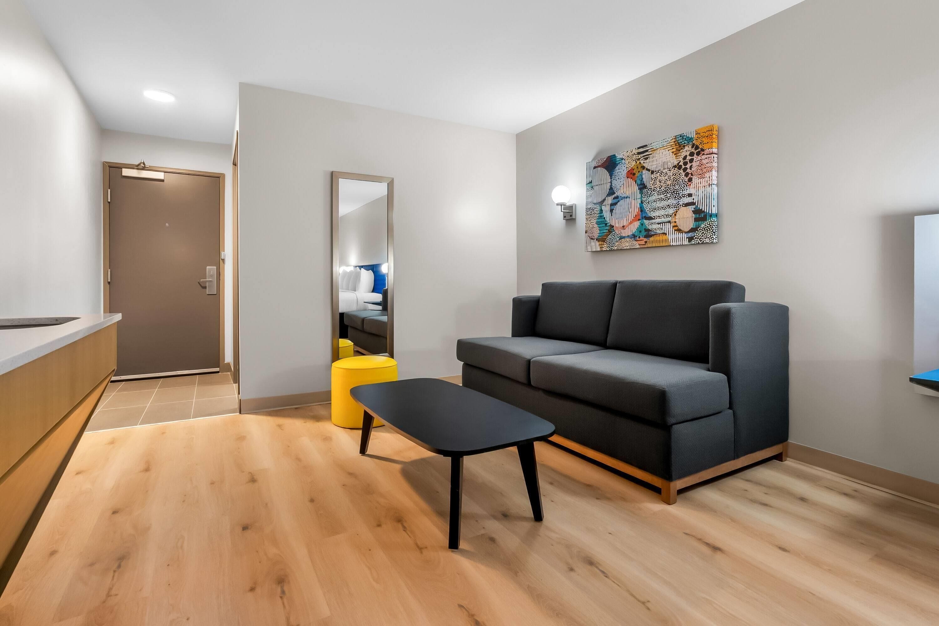 A modern living room with a sofa, a coffee table, and a yellow ottoman.