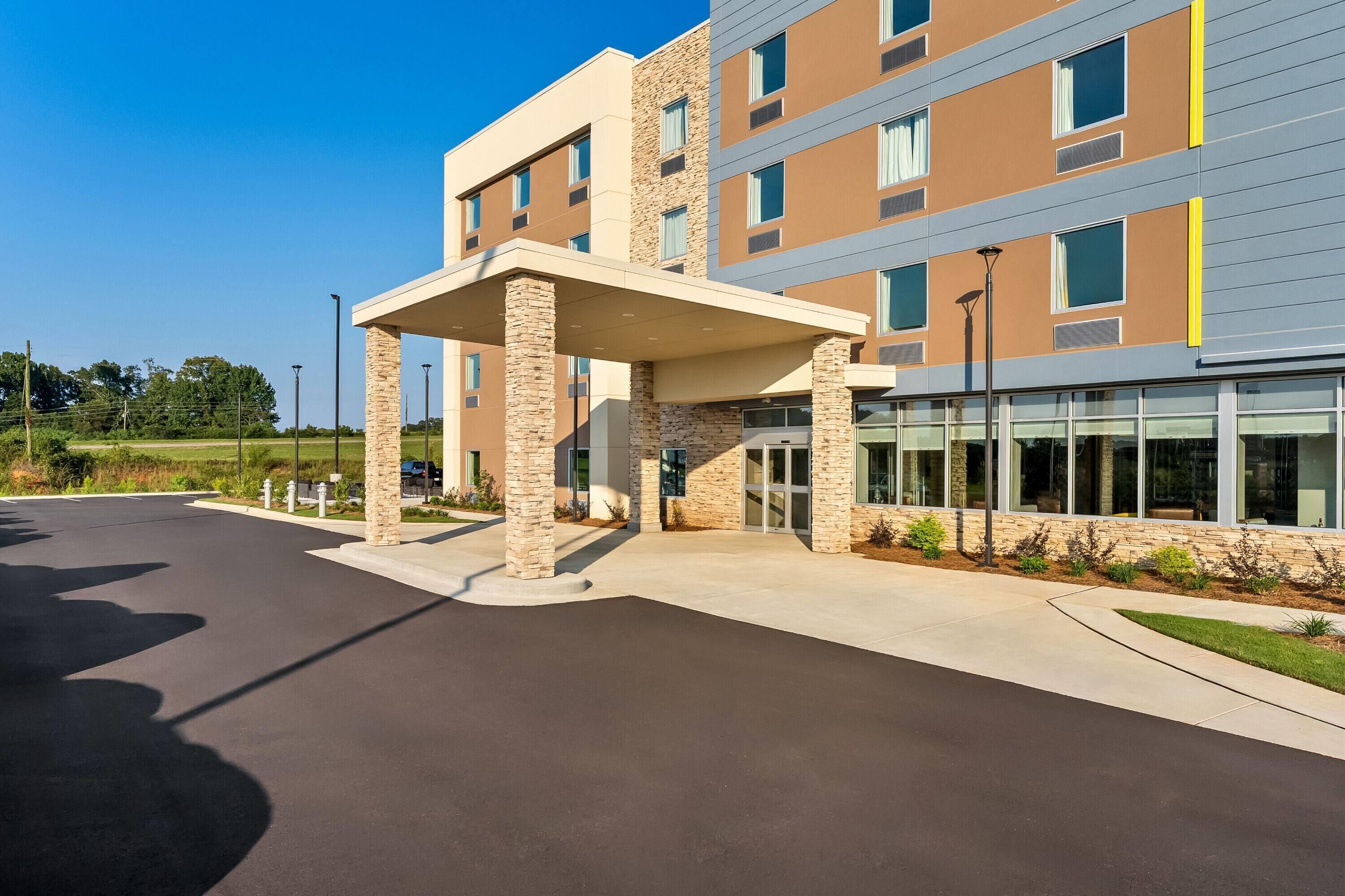 A multi-story hotel with a covered entrance, outdoor seating area, and a landscaped garden.
