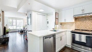 A modern kitchen with white cabinetry, a stainless steel dishwasher, and a built-in oven. - Modern & Bright Downtown Haven ~ Pool ~ Gym ~ Pkg! (Vancouver)