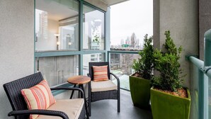 A balcony with wicker chairs and a small table, large windows, and potted plants. - Modern & Bright Downtown Haven ~ Pool ~ Gym ~ Pkg! (Vancouver)