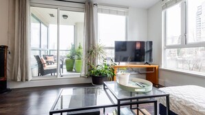 A modern hotel room with a glass coffee table, a bed, a TV, and a balcony with outdoor seating. - Modern & Bright Downtown Haven ~ Pool ~ Gym ~ Pkg! (Vancouver)