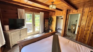 A wooden cabin bedroom with a bed, a television on a cabinet, and a sliding glass door leading to an outdoor area.