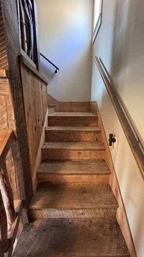 A wooden staircase with a handrail, leading to a landing with a light switch and a wall-mounted electrical outlet. - Rare 12-Guest Cabins w/ Hot Tubs, Fire Pits & Pets (Mariposa)