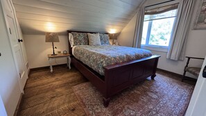 A bedroom with a wooden bed, two bedside tables, a nightstand, a window with curtains, and a patterned rug.