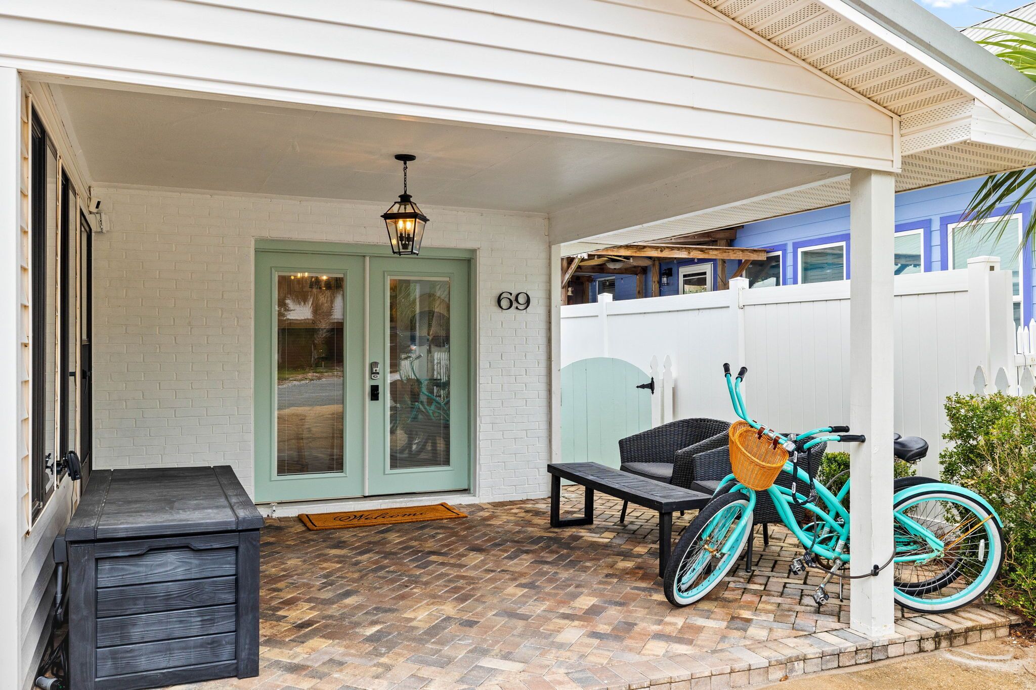 A covered porch with a teal bicycle, a bench, and a door marked with the number 69.