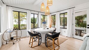 A spacious room with a round table, wicker chairs, and large windows offering a view of greenery. - Charming Blue Mountain Bungalow in 30A. Walk or Golf Cart down to the sand.  (Santa Rosa Beach)