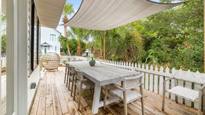 A wooden deck with a table and chairs, surrounded by a white picket fence and lush greenery. - Charming Blue Mountain Bungalow in 30A. Walk or Golf Cart down to the sand.  (Santa Rosa Beach)
