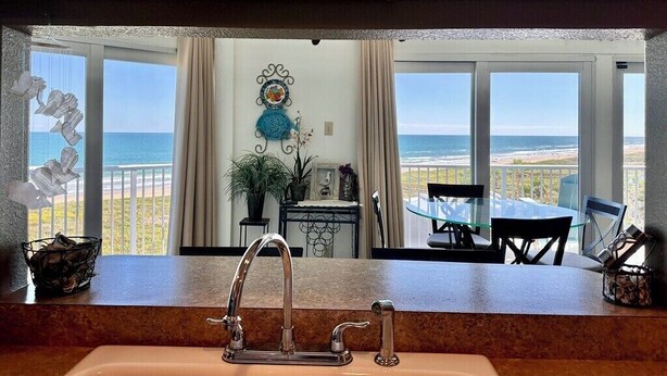 Una cocina con vista a la playa, un comedor con mesa y sillas, y un adorno en la pared.
