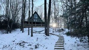 Une cabane en bois entourée d’arbres, avec un sentier enneigé qui y mène.