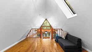 Une chambre à coucher aménagée dans un espace de type « loft », avec un plancher en bois, un canapé noir et une lucarne.