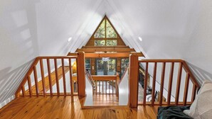 Un escalier en bois mène à une chambre située en mezzanine, qui est dotée d’une grande fenêtre.