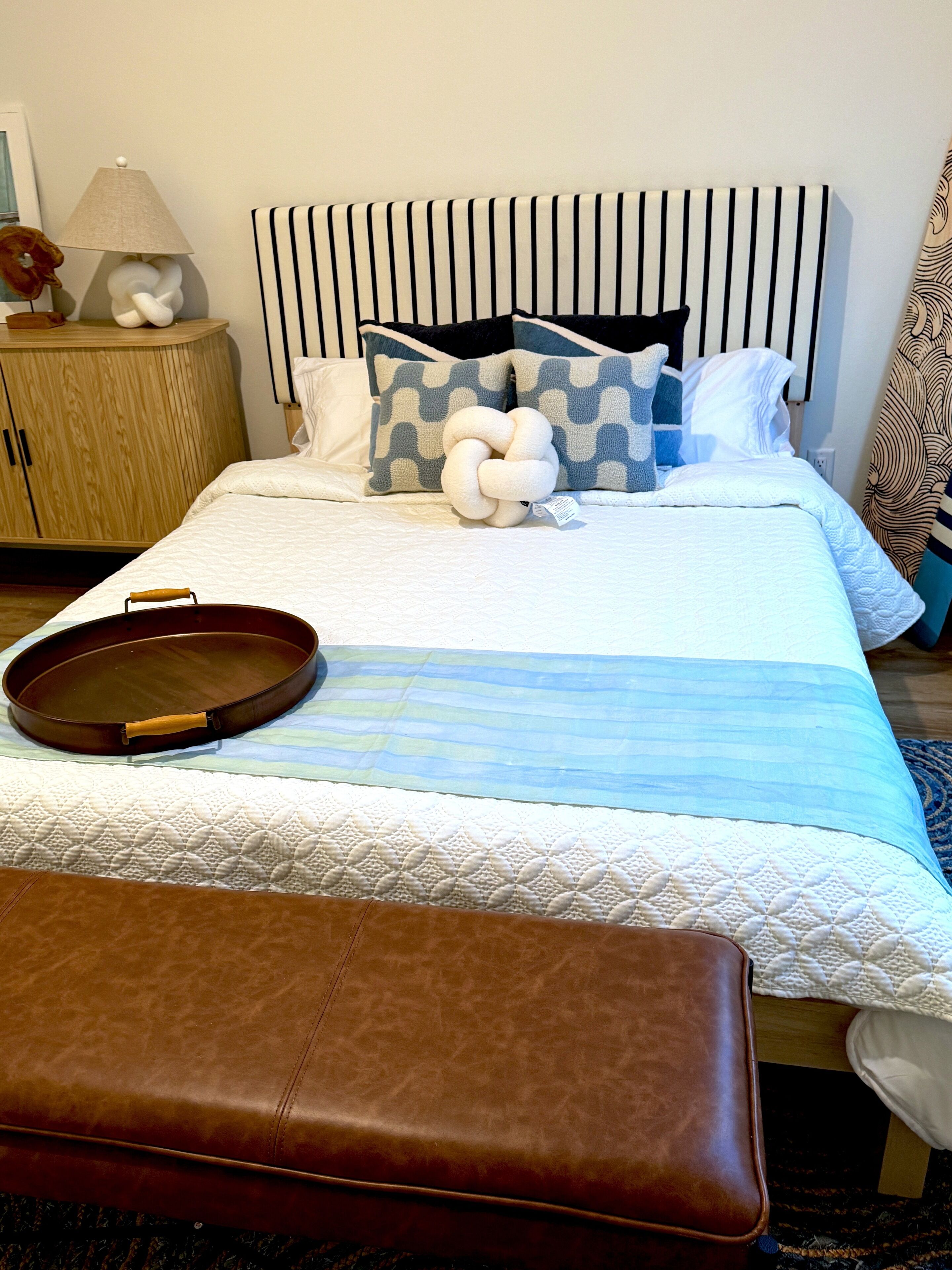 Una cama bien hecha con una colcha a rayas, una almohada decorativa y una bandeja sobre la cama.