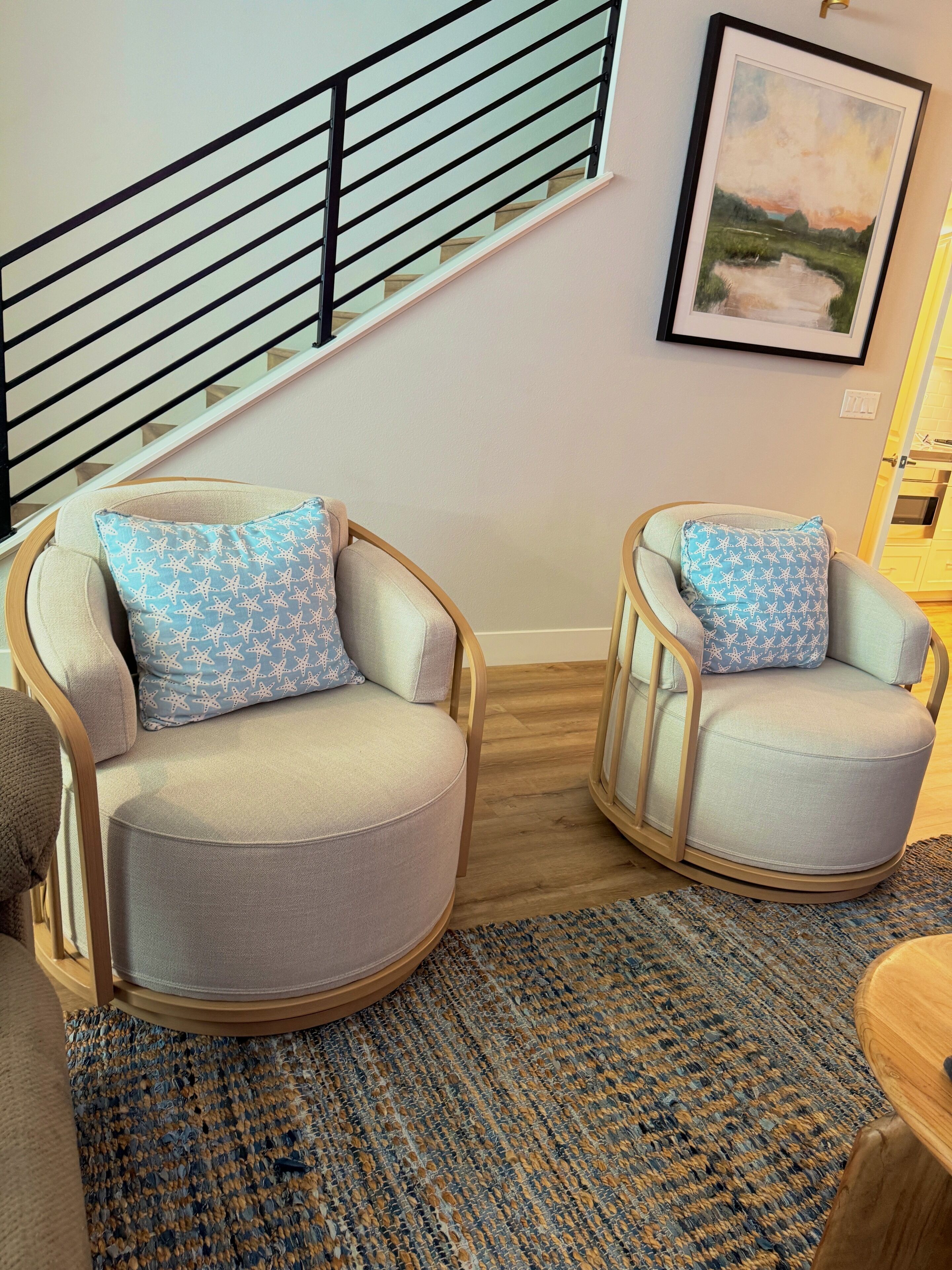 Una sala moderna con dos sillones, un tapete estampado y una escalera con barandilla.