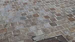 Un edificio con patio empedrado de piedra, puertas dobles de madera y un pequeño balcón con plantas en macetas.