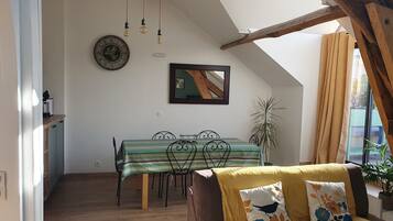 Une pièce chaleureuse avec une table à manger, un canapé agrémenté de coussins à motifs floraux, une horloge et un miroir au mur.