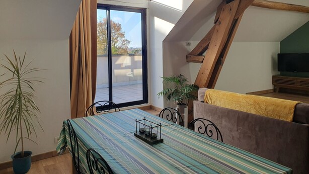 Una habitación acogedora con una mesa de comedor, sillas, un sofá, un televisor y un gran ventanal con cortinas.