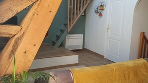 Una habitación estilo loft con vigas de madera a la vista, una escalera, una puerta blanca y una manta amarilla sobre un sofá.