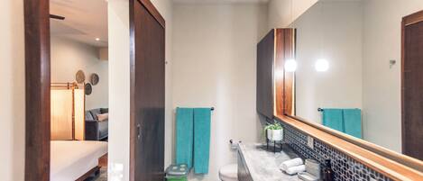 Un baño moderno con un espejo grande, un inodoro, un lavabo y una zona de ducha.