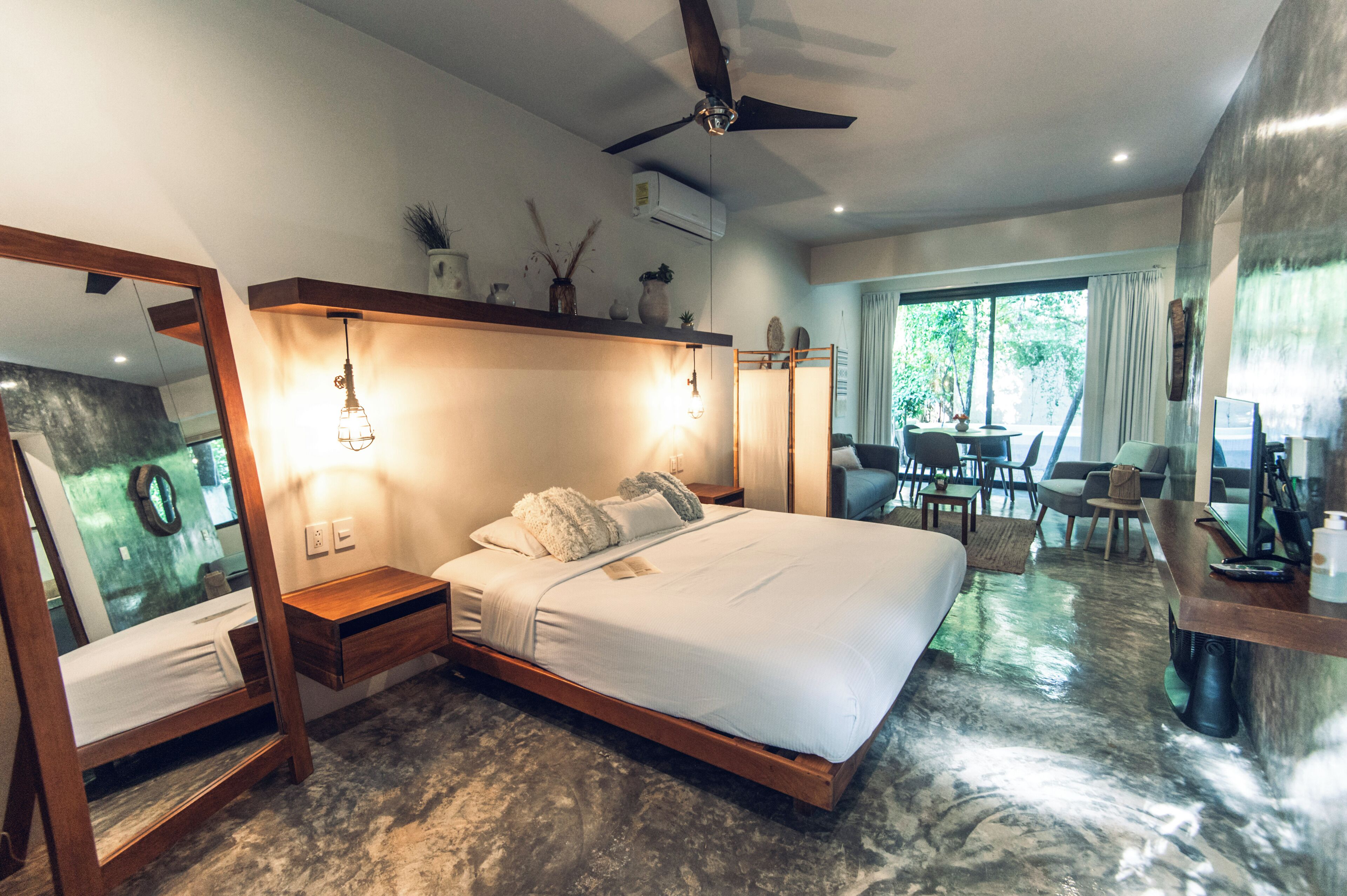A modern bedroom with a large bed, bedside tables, a ceiling fan, and a view of the outdoors.