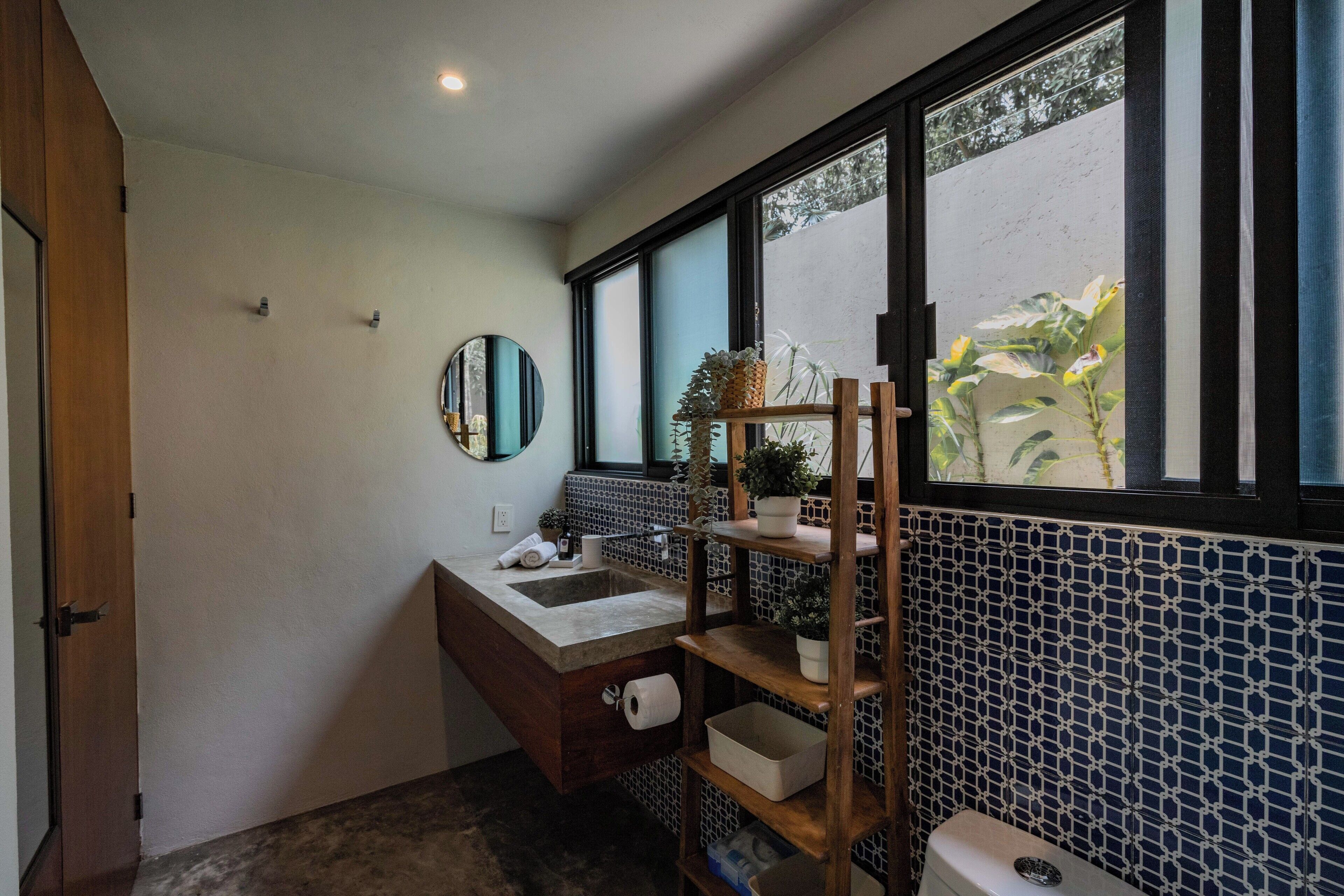 A bathroom with a wooden vanity, a mirror, a sink, a toilet, and a window with a view of greenery.