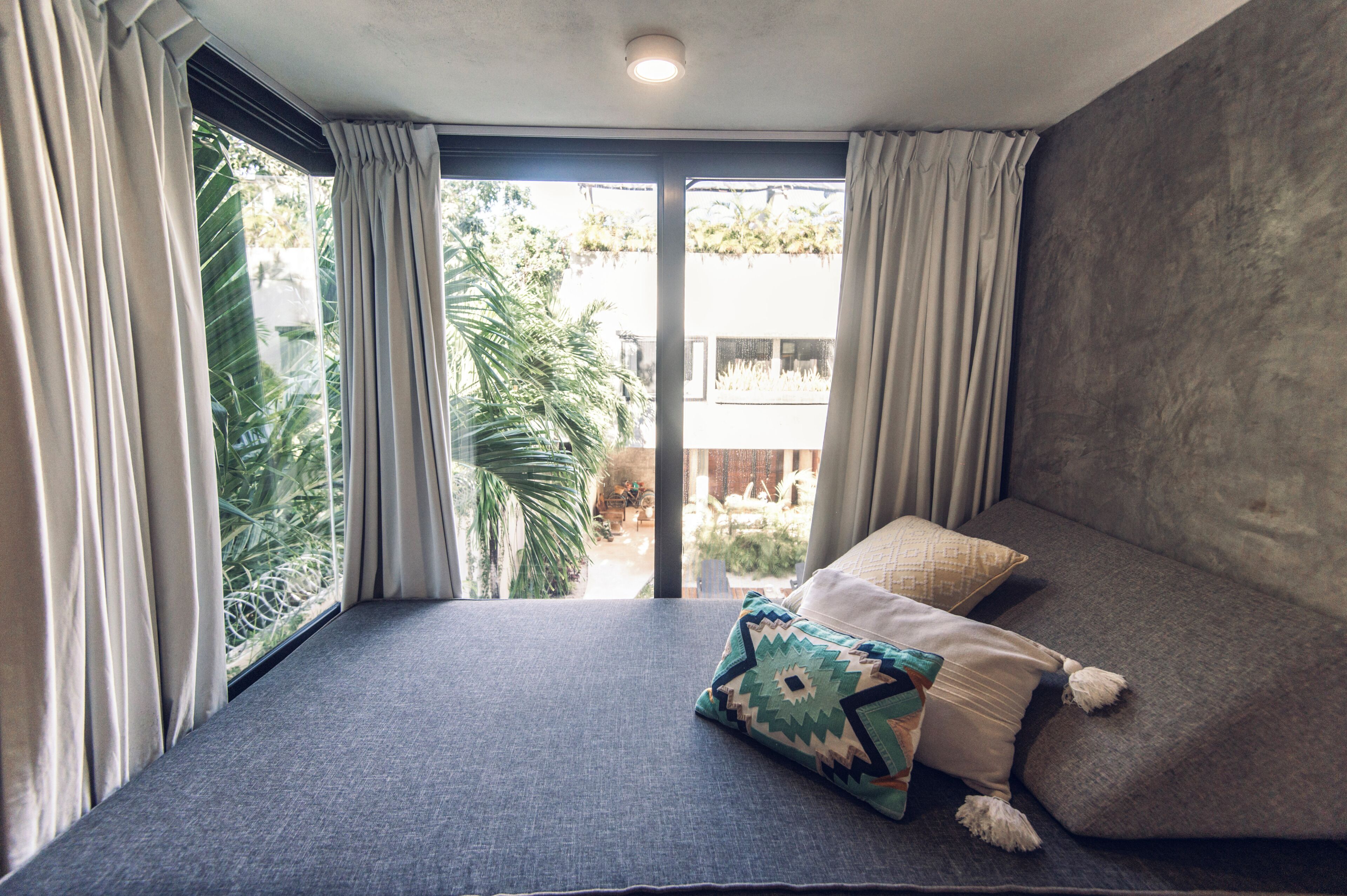 A room with a large window, a grey sofa, and a patterned pillow.