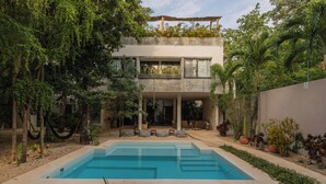 Una casa moderna con piscina, mobiliario exterior y abundante vegetación.
