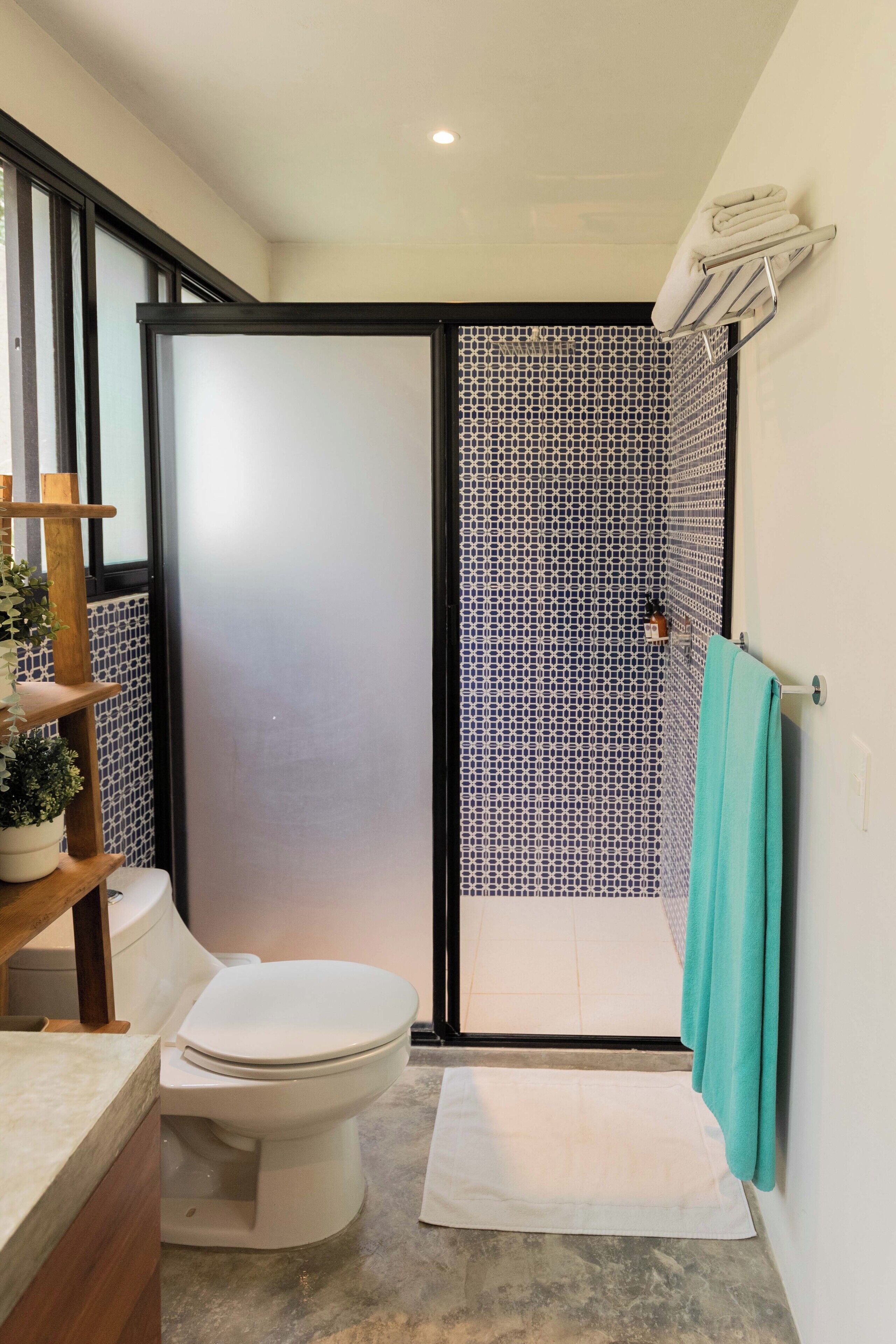 Une salle de bain comprenant des toilettes, un lavabo, un porte-serviettes et un espace douche avec un rideau à motifs.
