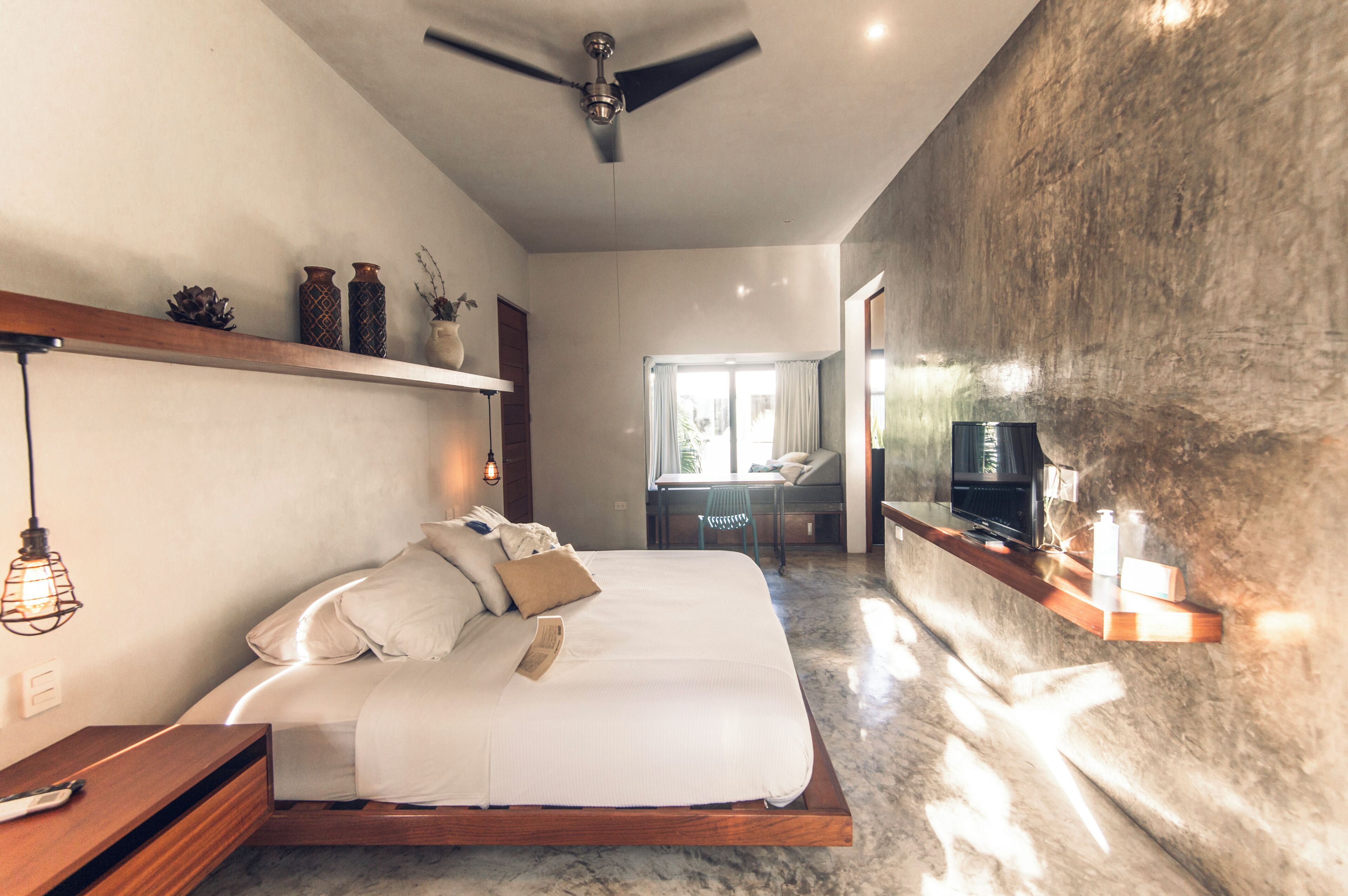 Un dormitorio moderno con una cama grande, ventilador de techo, televisor y vistas al exterior.
