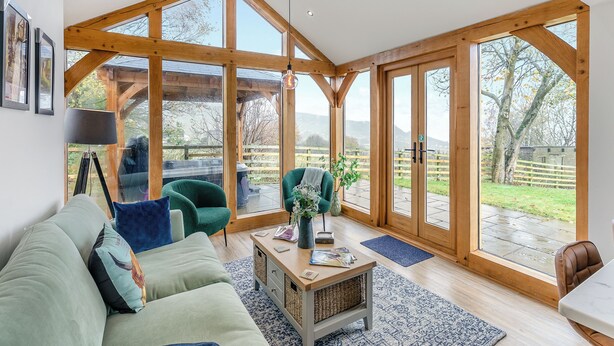 Una habitación amplia con techo alto, ventanas grandes, un sofá verde, una mesa de centro de madera y vistas al exterior.