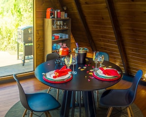 A dining table set for two with a view of a wooden deck and greenery outside. - Vila nas Montanhas (Anitapolis)