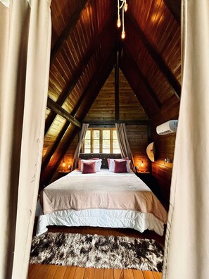 A cozy attic bedroom with a sloped ceiling, a large bed with white bedding, and a rustic wooden floor. - Vila nas Montanhas (Anitapolis)