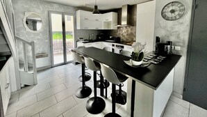 Una cocina moderna con una isla central, taburetes de bar, iluminación colgante y un reloj en la pared.
