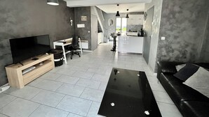 Una sala de estar moderna con televisor, mueble de madera para equipo audiovisual, una mesa de centro negra y un sofá de cuero negro.