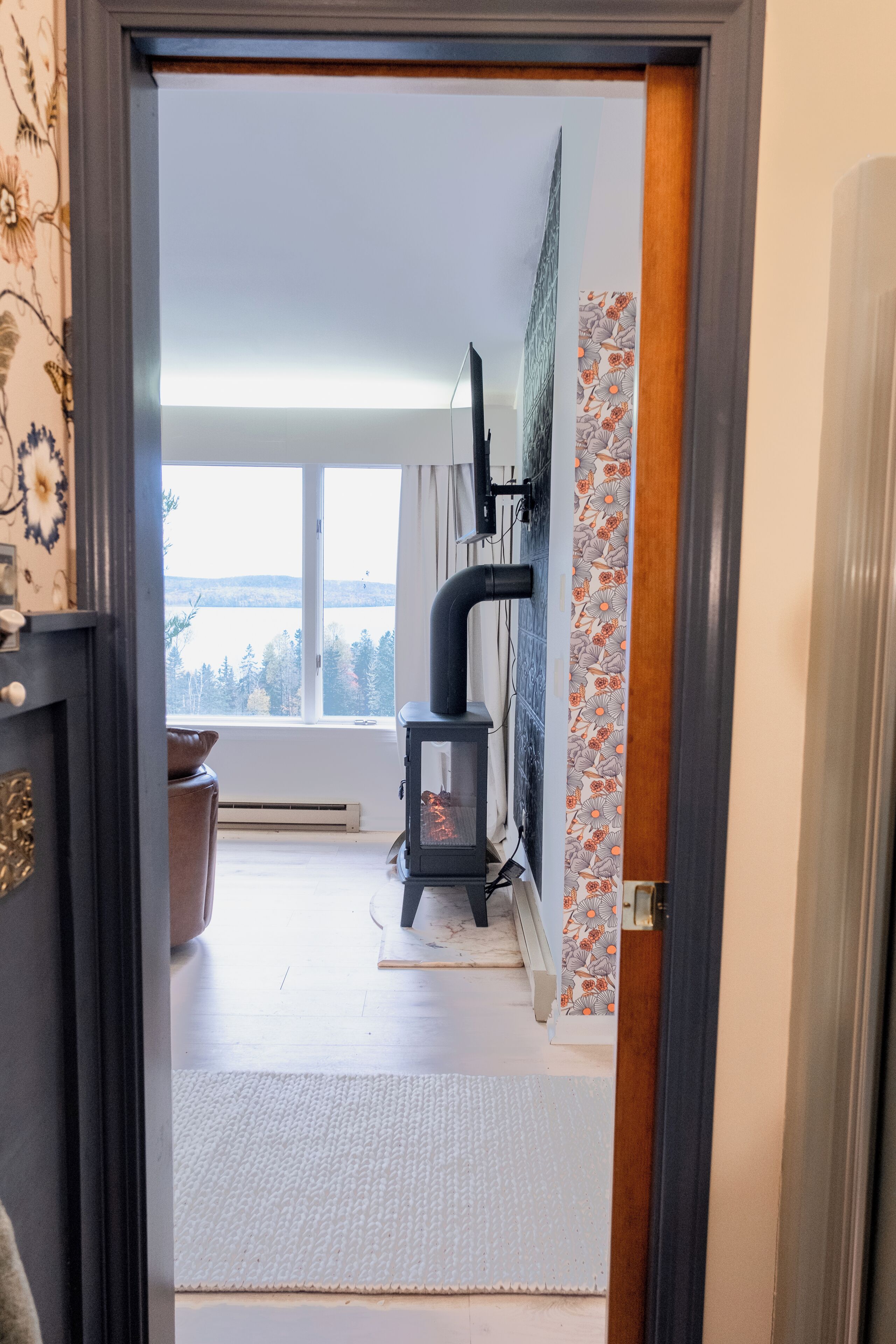 Een kamer met een groot raam, een open haard en uitzicht op een meer.