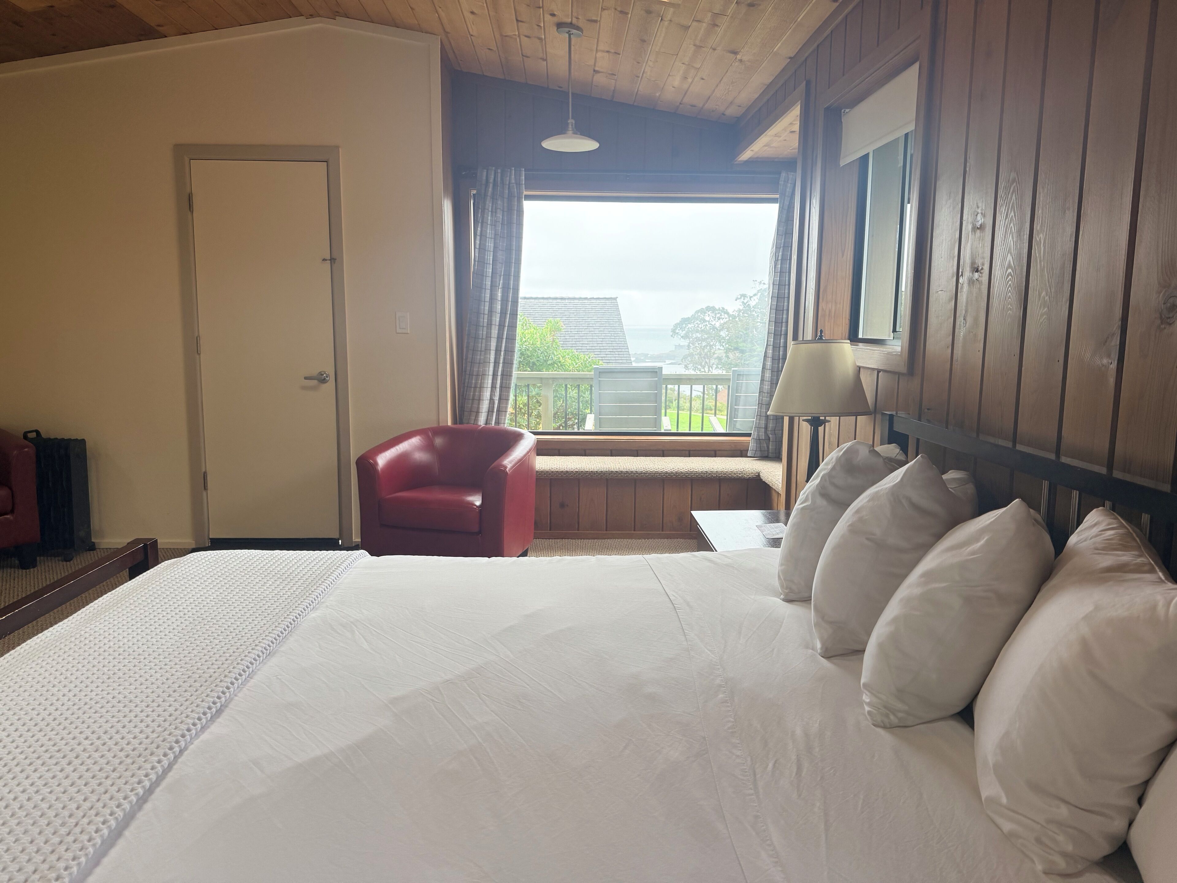 Habitació d'hotel amb un llit gran, una cadira vermella, una finestra amb vista i un sostre de fusta.