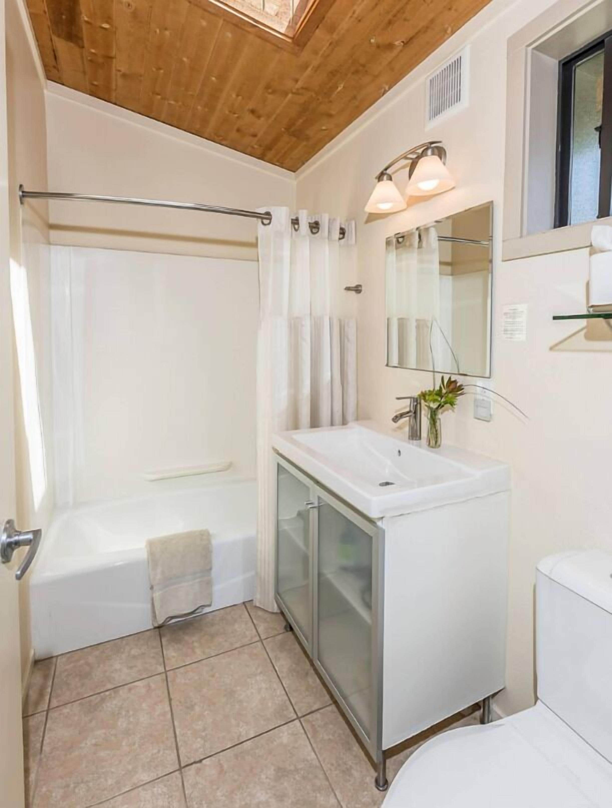 A bathroom with a bathtub, a glass-enclosed vanity, a mirror, and a shower curtain.