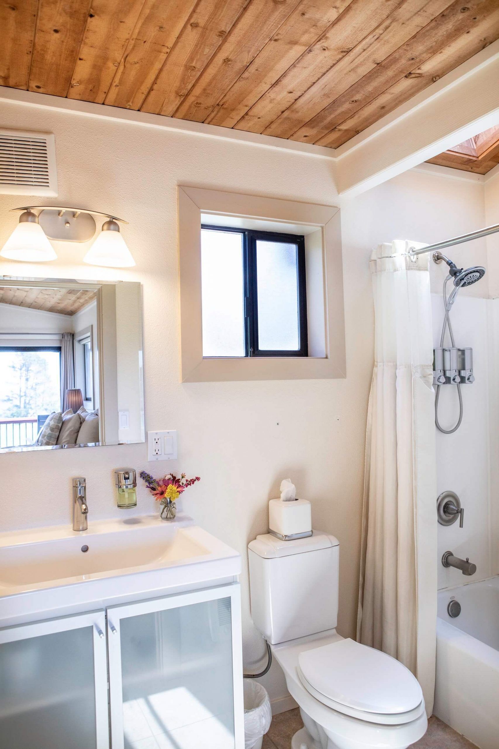 Un baño con techo de madera, ventana, lavamanos, inodoro y ducha.