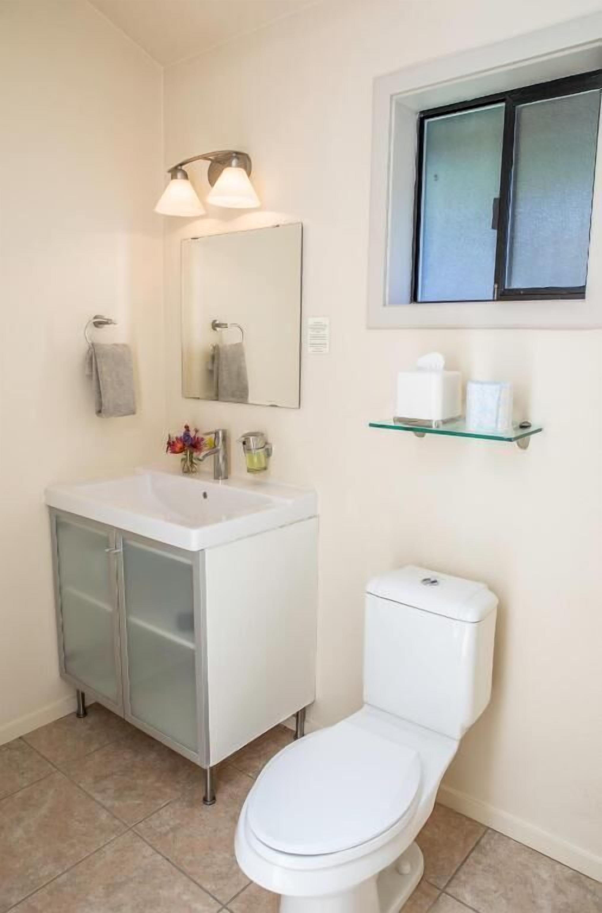 A bathroom with a white sink, a mirror, a toilet, and a window above the toilet.