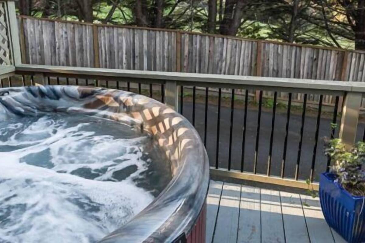 Un jacuzzi en una terraza de madera con un cerramiento de celosía al fondo.