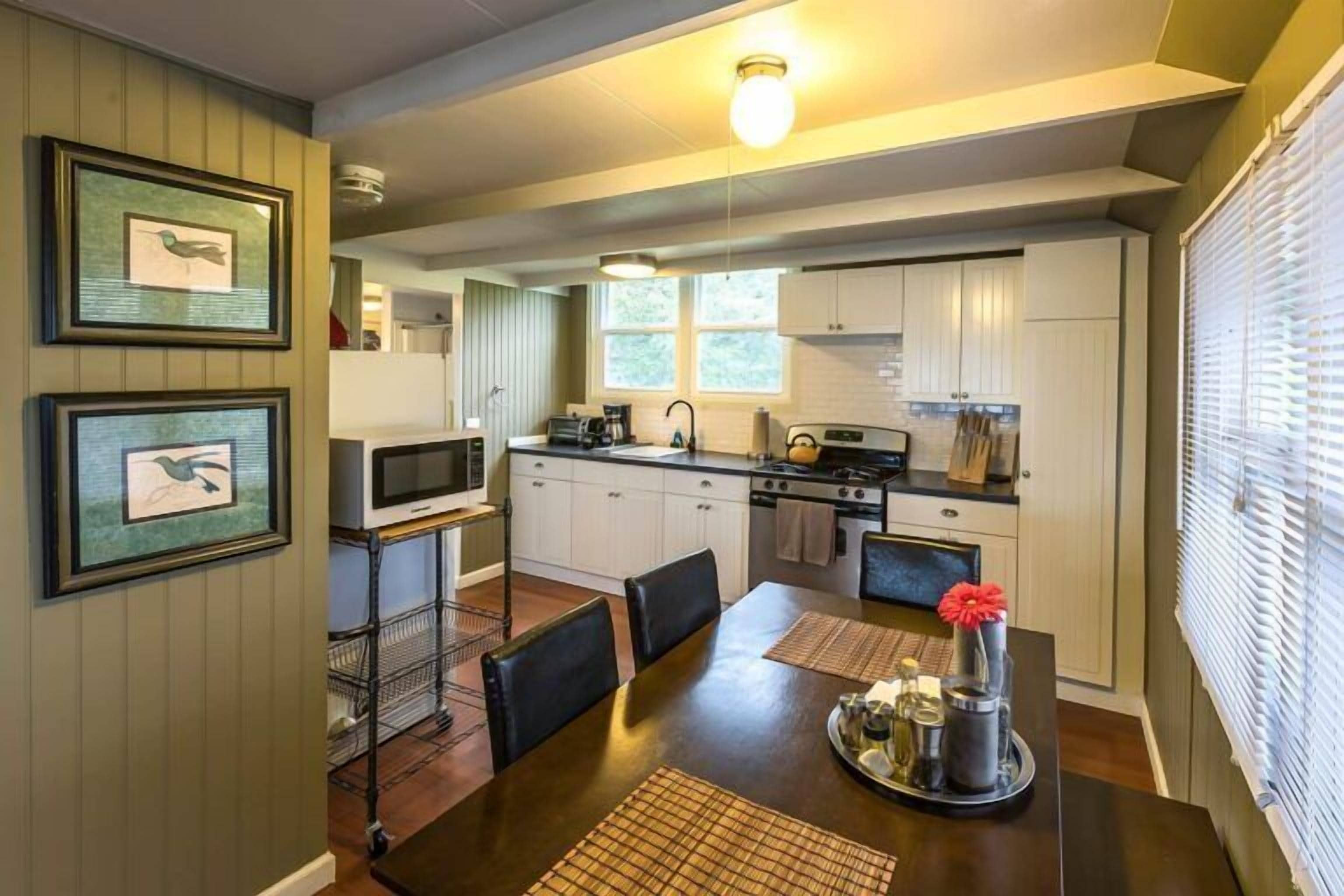 A modern kitchen with white cabinets, a dining table with chairs, and a TV on a stand.