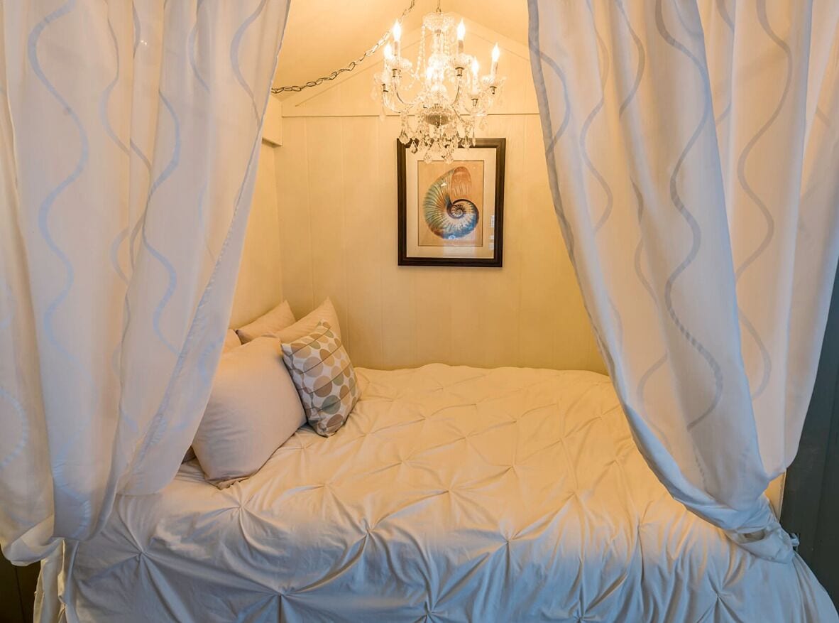 A bedroom with a canopy bed, a chandelier, and a framed artwork on the wall.