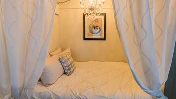 A bedroom with a canopy bed, a chandelier, and a framed artwork on the wall.