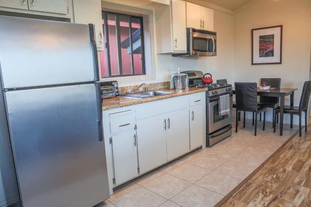 A compact kitchen with a refrigerator, microwave, stove, and sink. There is a dining area with a table and chairs.