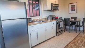 A compact kitchen with a refrigerator, microwave, stove, and sink. There is a dining area with a table and chairs.