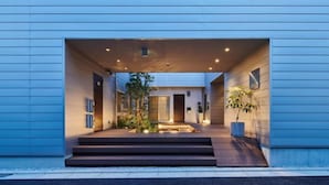 A modern building with a flat facade, a central entrance with steps, and a small garden area with plants. - Reikyo Garden Osaka (Osaka)